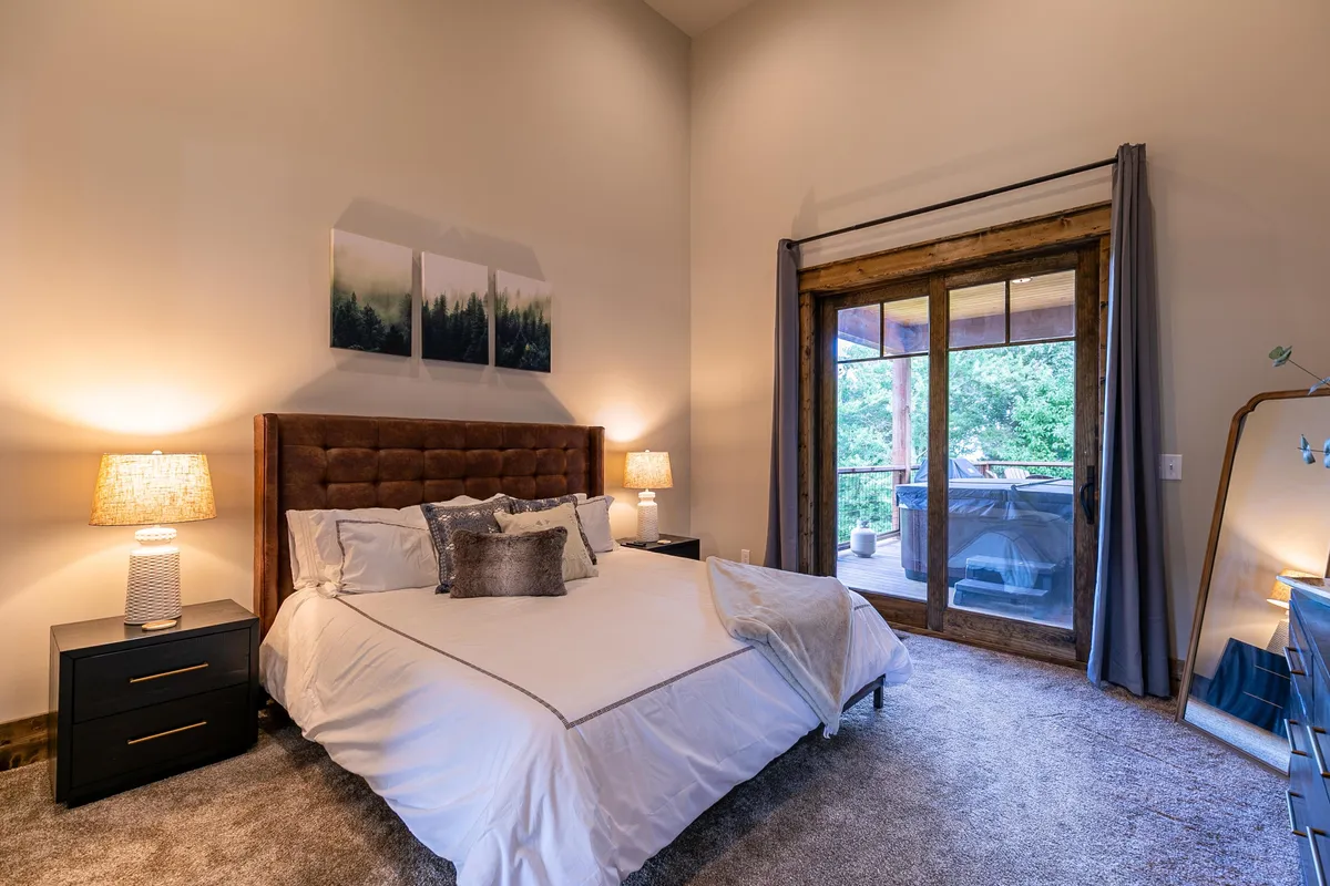 A serene bedroom featuring a plush headboard, large windows leading to a private balcony, and tasteful decorative pillows. Ambient lighting from nightstands creates a restful atmosphere, and abundant natural light streams in through the windows, offering a tranquil space for relaxation or a peaceful night's sleep.