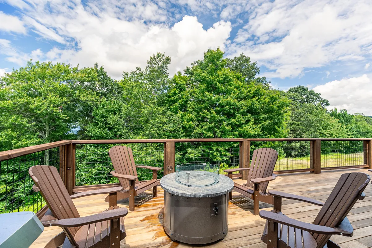 A cozy wooden deck nestled among the trees, furnished with Adirondack chairs gathered around a gas fire pit. The area feels sheltered and intimate, perfect for evening gatherings, storytelling, and enjoying the warmth of a fire under the night sky.