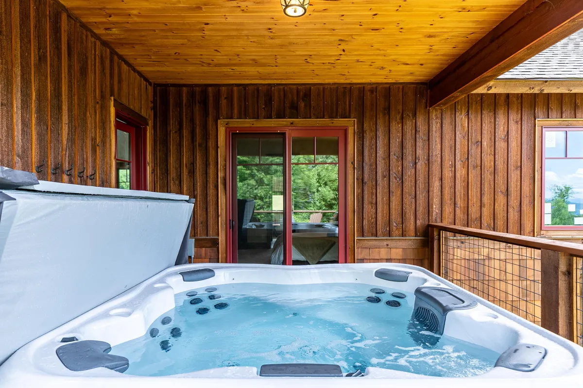 This image captures a cozy hot tub nestled against warm wooden walls, with glass doors that open out to the mountain scenery. The setting is intimate and tranquil, offering a sense of privacy and luxury perfect for couples. The inviting hot tub is the focal point, suggesting evenings spent stargazing or unwinding together.