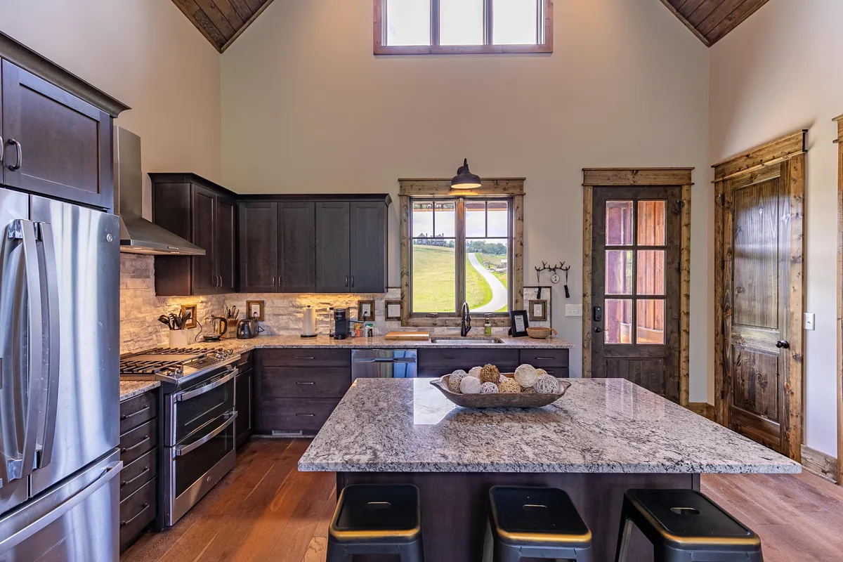 A spacious kitchen scene with a granite island, black cabinetry, large windows framing scenic vistas, and top-of-the-line stainless steel appliances. The setup suggests a welcoming atmosphere ideal for gatherings and group meal prep, with plenty of surface space for cooking or casual breakfasts.