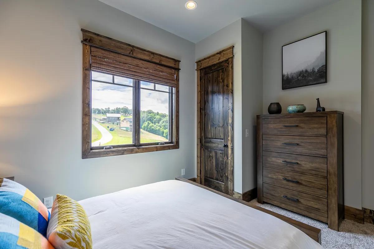 This image presents a serene bedroom with a colorful bed, wooden dresser, and a window that frames beautiful views. Soft lighting and cozy decor create a peaceful mood, while the window invites a sense of connection to the outdoors, perfect for sharing a quiet moment together while enjoying the mountain landscape.