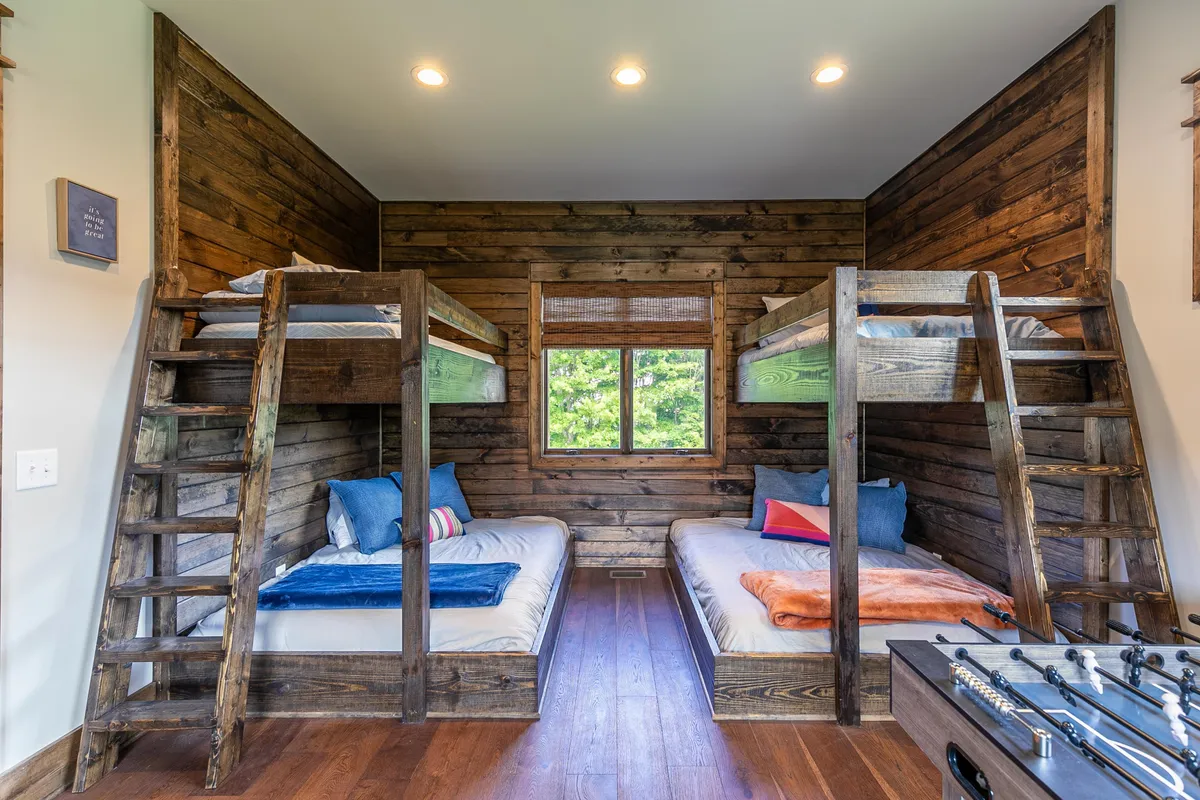 A cheerful bunk room interior with multiple bunk beds, a foosball table, and a window letting in natural light. The playful setup invites kids to unwind, play games together, or gather for cozy storytelling. The foosball table promises friendly competition and fun indoor moments for young guests.