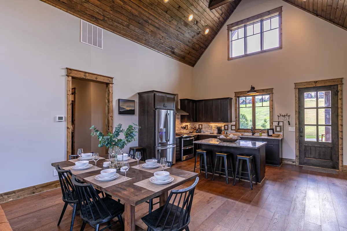 A dining area set for a meal, seamlessly connected to a large kitchen island and an open door that leads outside. The view captures the easy flow between kitchen, dining, and outdoor living, underlining the social and functional facets of the culinary space.